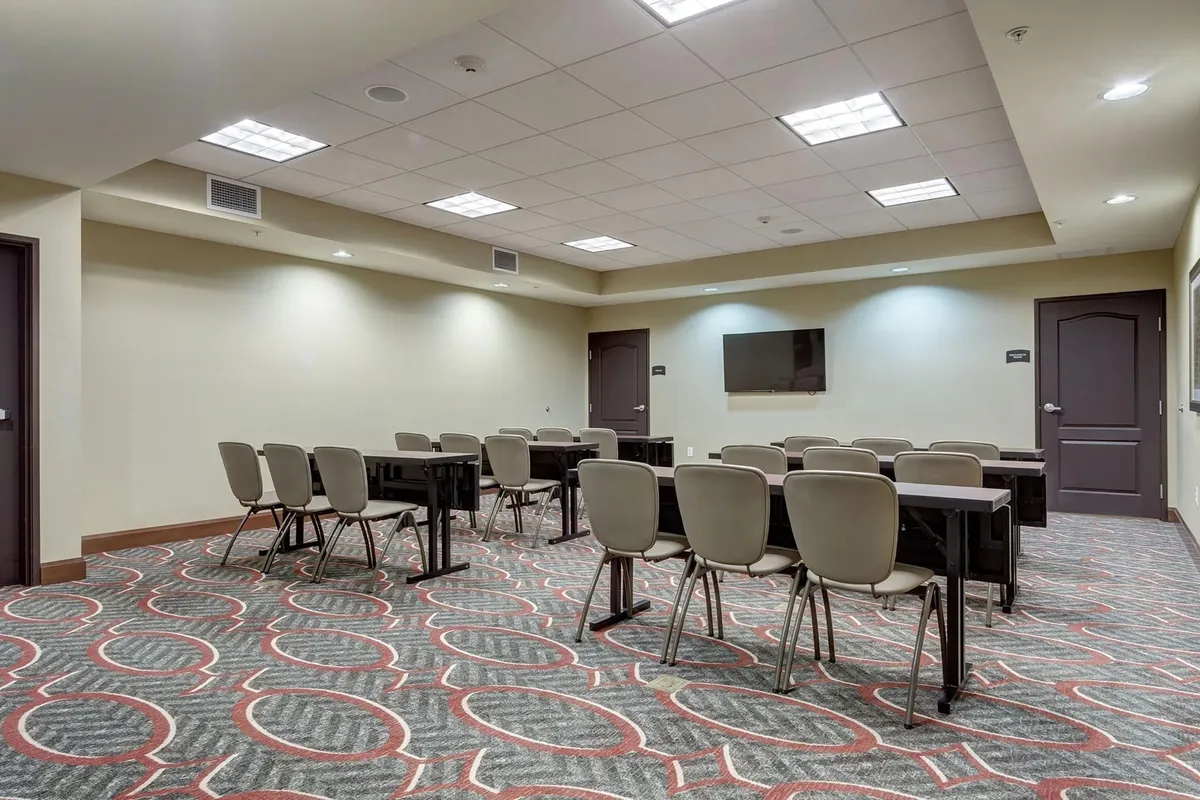 This image showcases a modern, well-equipped business center with tables, chairs, and a screen, creating a focused, collaborative atmosphere ideal for meetings, workshops, and professional development. The setting appears inviting for both team discussions and individual productivity.