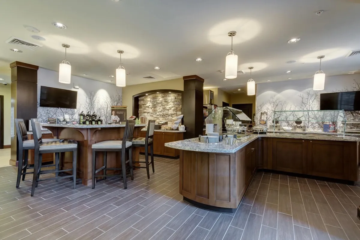 The scene focuses on a central bar area with a stone feature wall and a display counter, set up for dining and socializing. The arrangement encourages guests to gather for meals, snacks, or coffee in a relaxed setting.