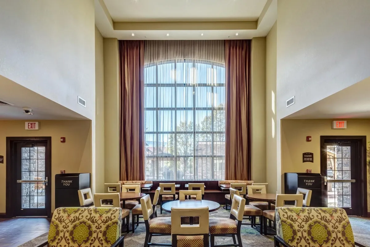 An airy seating area illuminated by a large arched window, with decorative curtains and cozy furniture. Sunlight streams in, creating an inviting, comfortable environment ideal for reading, casual conversations, or enjoying a cup of coffee.