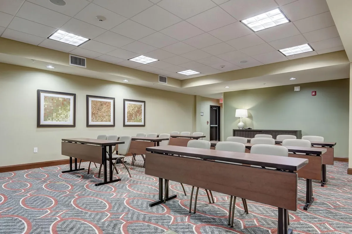 This interior scene presents a flexible communal space with tables and chairs, framed artwork on the wall, and cozy lighting. The setup supports a range of activities from meetings to social guest receptions, emphasizing collaboration and interaction.