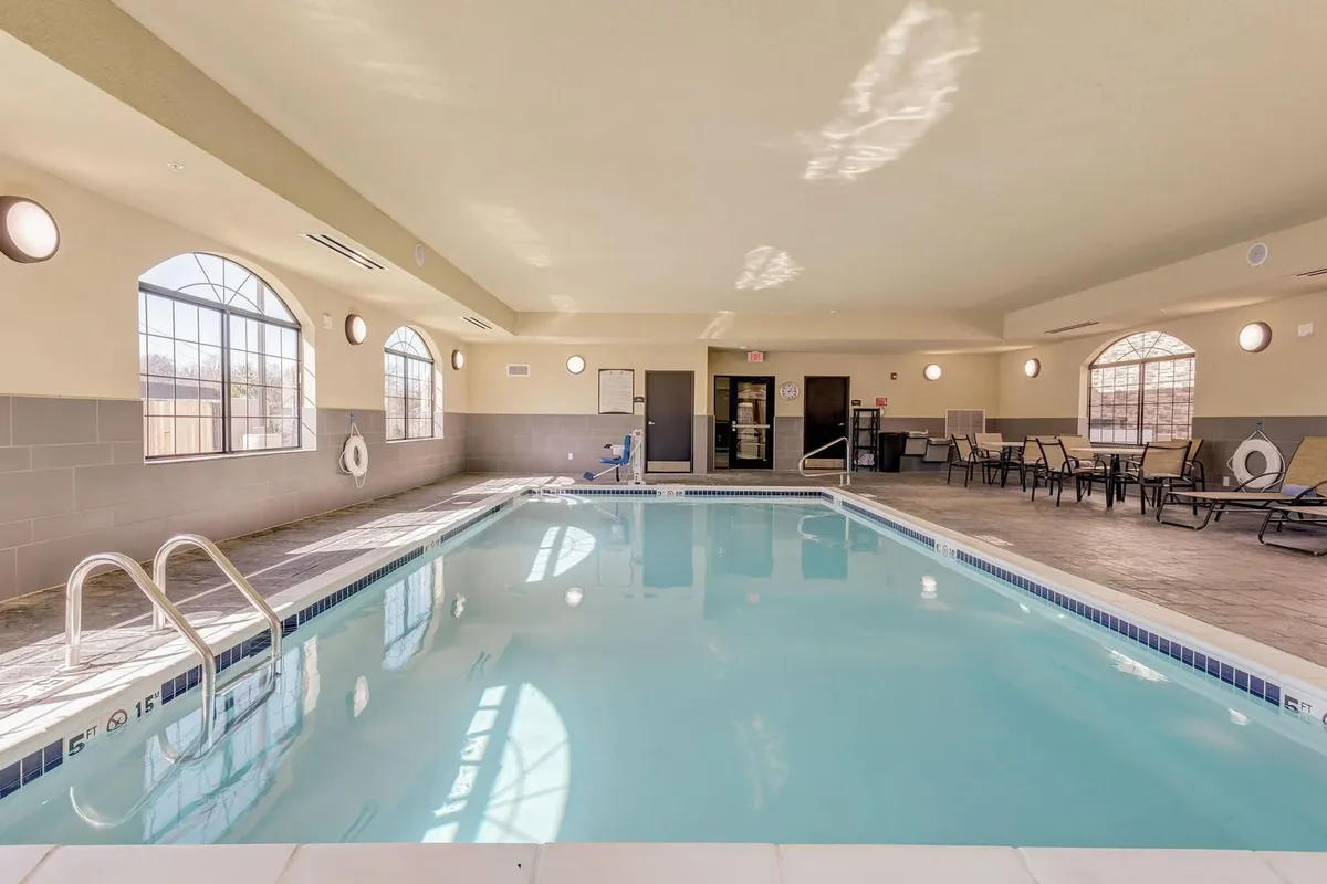This scene features another angle of the indoor pool, highlighting large windows, comfortable poolside seating, and guests enjoying a sunny day. The mood is tranquil and enjoyable, suggesting opportunities for gentle socializing, relaxation, or a change of scenery without leaving the property.