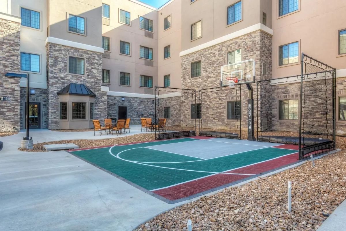 A vibrant exterior shot of a basketball court adjacent to a modern building, with comfortable seating areas nearby. The scene is lively, suggesting opportunities for friendly basketball games, evening barbecues, and casual socializing—activities that appeal to families seeking outdoor fun and connection.